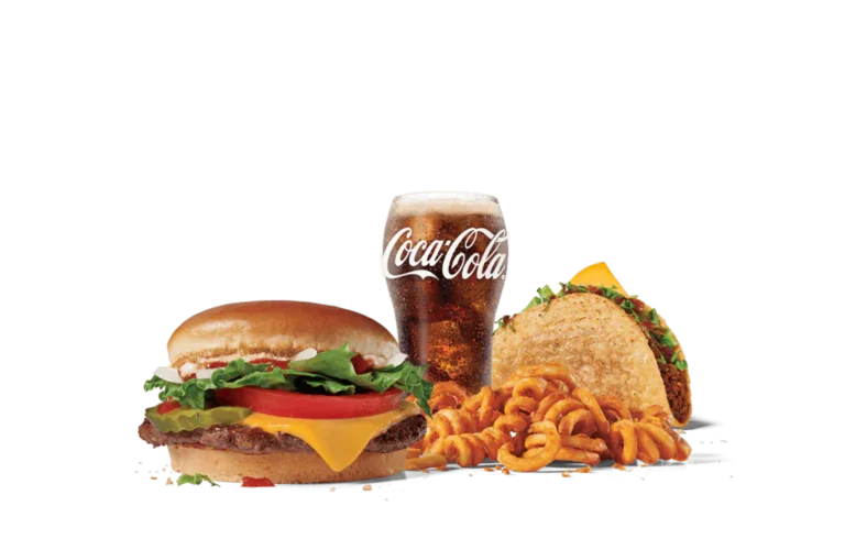 A fast food meal featuring a junior cheeseburger with lettuce, tomato, and mayonnaise, a taco filled with beef and topped with lettuce, curly fries, and a cold glass of Coca-Cola, all set against a transparent background.