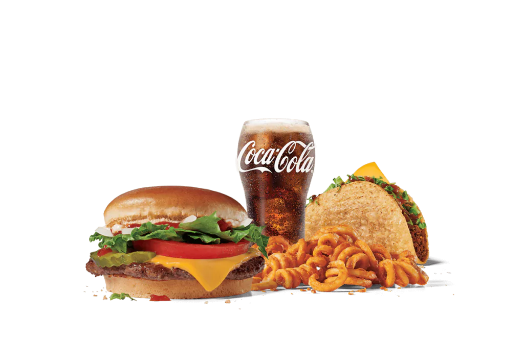A fast food meal featuring a junior cheeseburger with lettuce, tomato, and mayonnaise, a taco filled with beef and topped with lettuce, curly fries, and a cold glass of Coca-Cola, all set against a transparent background.
