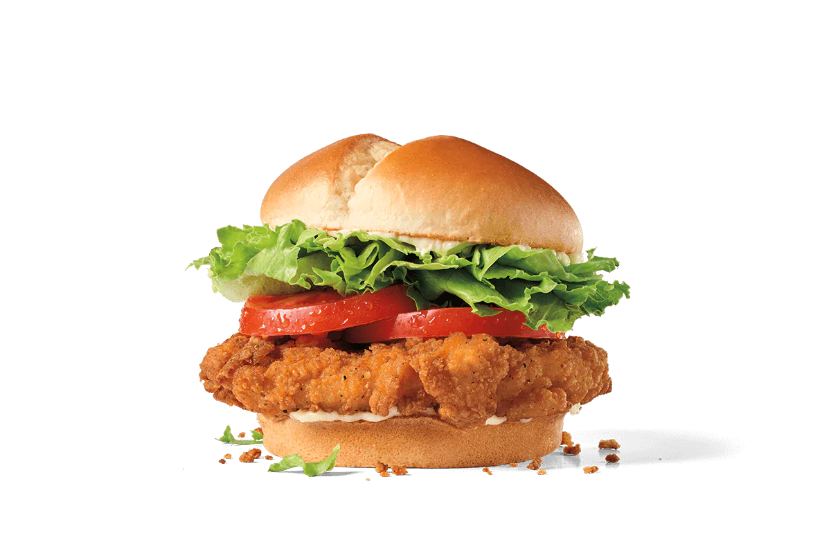 A stacked spicy chicken sandwich with a crispy breaded chicken patty, layers of fresh green lettuce, juicy tomato slices, and topped with a golden toasted bun, presented on a transparent background with crumbs scattered around.