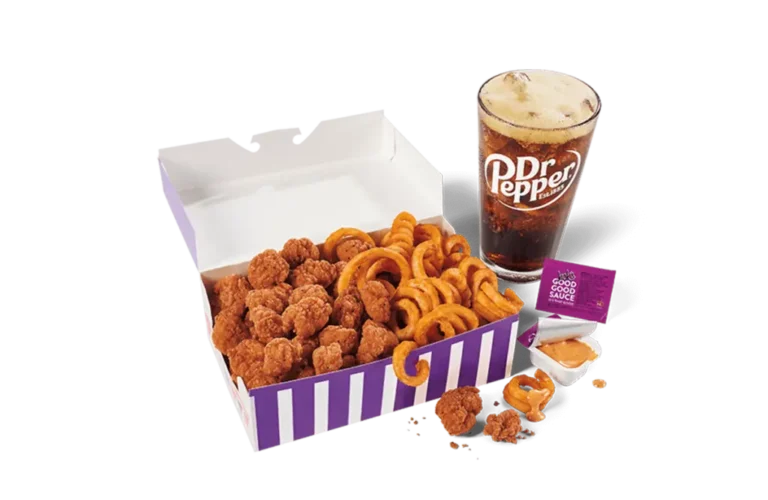 A large serving of spicy popcorn chicken and curly fries in a striped purple and white box, accompanied by a glass of Dr Pepper with a foamy head, and a sachet of sauce, presented on transparent background.