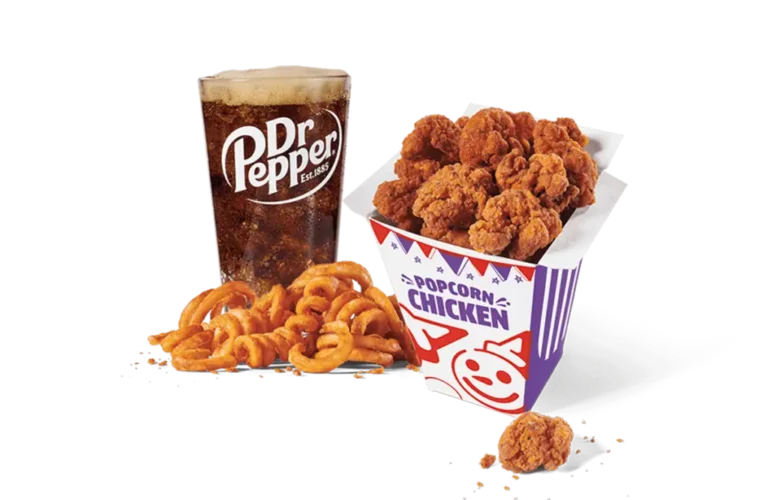 A box of crispy spicy popcorn chicken next to a heap of curly fries, accompanied by a glass of Dr Pepper, presented on transparent background. The meal is ideal for a quick, delicious snack or lunch.
