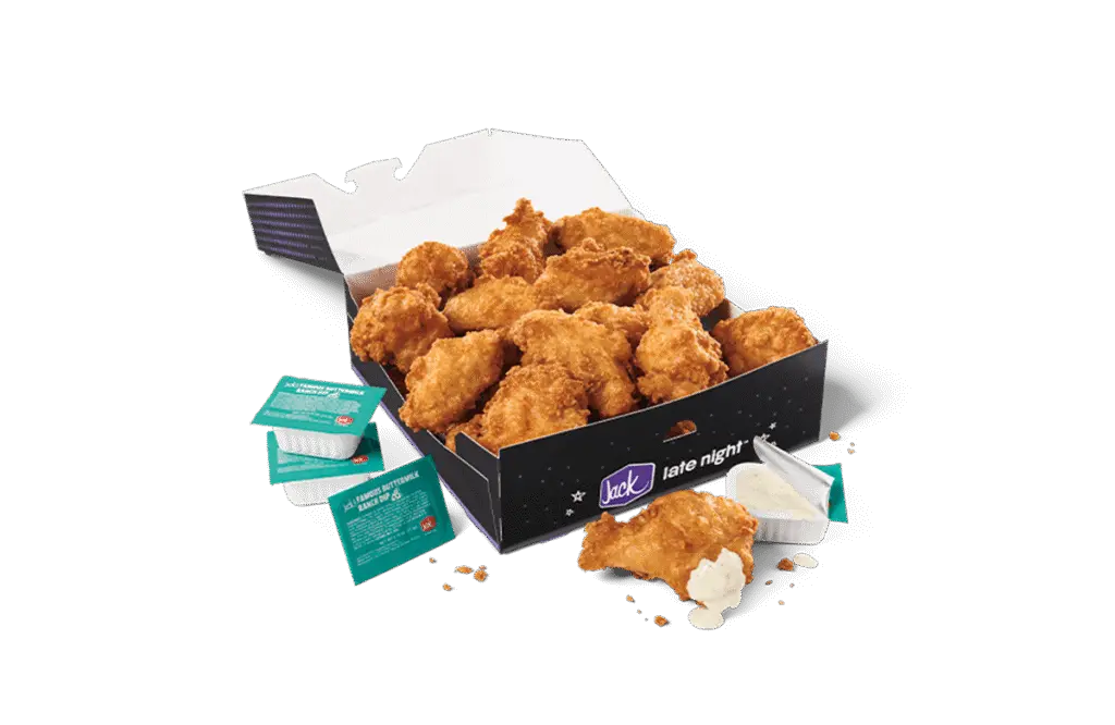 An 18-piece Classic Crispy Chicken Wings box from Jack in the Box, featuring golden, perfectly fried chicken wings. The wings are served in a sleek black box with the "Jack late night" branding. Surrounding the box are dipping sauces and condiment packets, including creamy ranch dressing, completing the meal's presentation.
