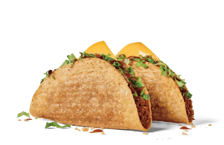 Two crunchy tacos filled with seasoned beef, shredded lettuce, and a slice of yellow cheese. The tacos are garnished with taco sauce and displayed side by side on a transparent background. Crumbs and pieces of lettuce are scattered around for a realistic touch.