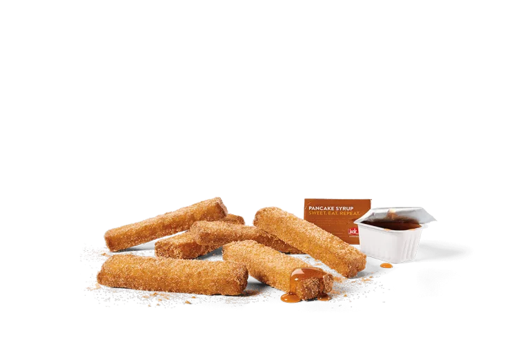 A pile of cinnamon sugar-coated French toast sticks with visible granules of sugar, next to a small white container of pancake syrup labeled 'Sweet. Eat. Repeat.', all set against a transparent background.