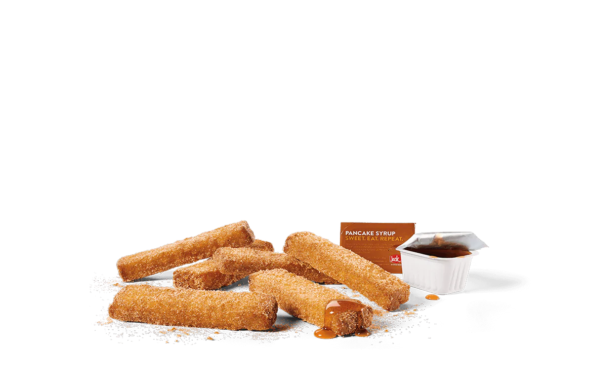 A pile of cinnamon sugar-coated French toast sticks with visible granules of sugar, next to a small white container of pancake syrup labeled 'Sweet. Eat. Repeat.', all set against a transparent background.
