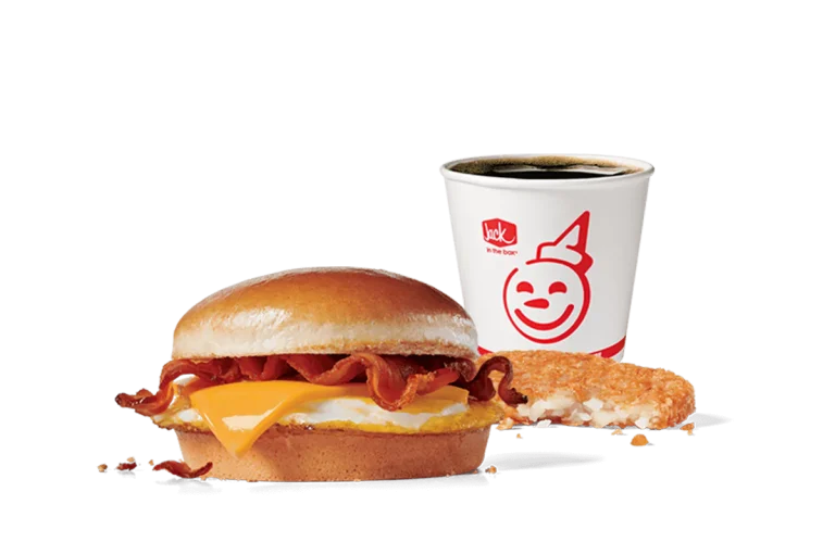 A mouthwatering Bacon Breakfast Jack® Combo from Jack in the Box featuring a sandwich with bacon, egg, and American cheese on a warm bun. Accompanied by a crispy hash brown and a cup of hot coffee, all presented against a plain green background.