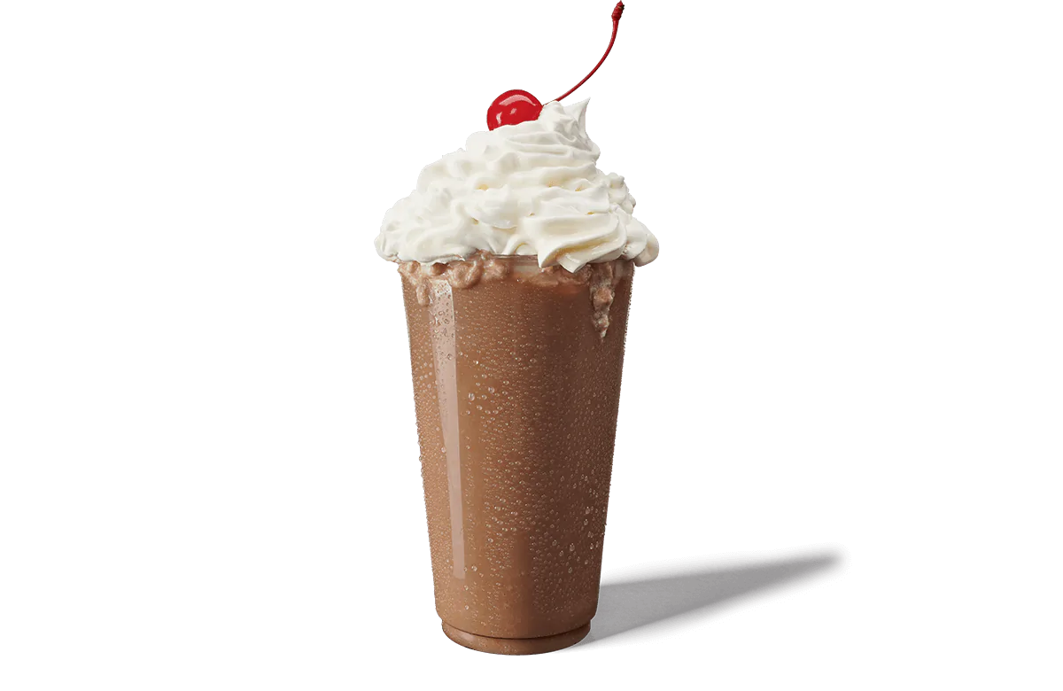 A tall glass filled with a rich chocolate shake, topped with a generous amount of whipped cream and garnished with a bright red cherry on transparent background. The glass is covered in condensation, indicating the coldness of the shake.