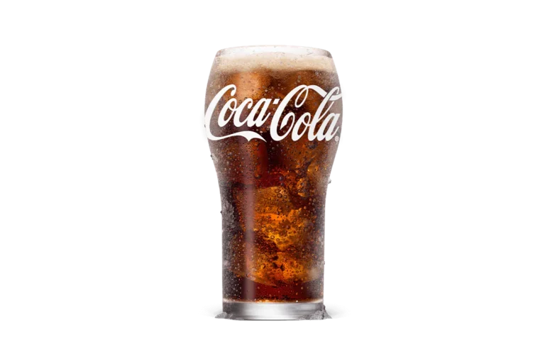 A tall glass of Coca-Cola® filled with ice cubes, featuring the signature dark and fizzy soda topped with a light foam layer, providing a refreshing drink experience.