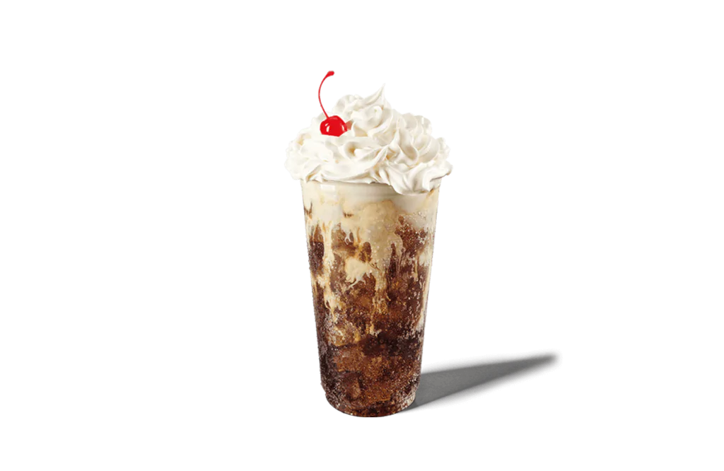 A tall glass filled with layers of dark soda and creamy vanilla, topped with a generous swirl of whipped cream and a bright red cherry. The drink has a frosty appearance, making it look indulgent and refreshing.