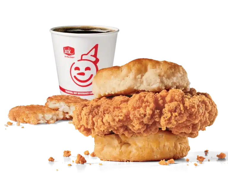 Promotional image of Jack in the Box's Homestyle Chicken Biscuit Combo featuring a crispy chicken fillet sandwiched in a soft biscuit, accompanied by a hash brown and a coffee cup with the red Jack in the Box logo. The chicken's crunchy coating and flaky biscuit are highlighted against a transparent background, showcasing a popular breakfast choice.