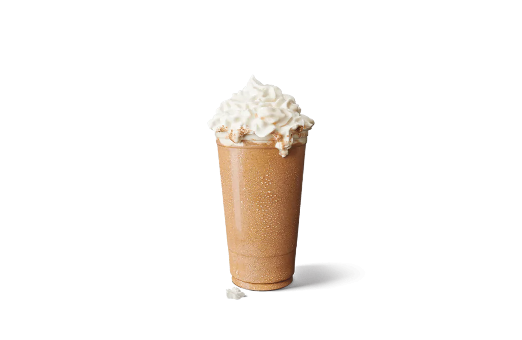 A tall glass filled with a frosty caramel-flavored iced creamaccino, topped generously with whipped cream. The drink showcases condensation droplets on the glass, indicating its chilled and refreshing nature.