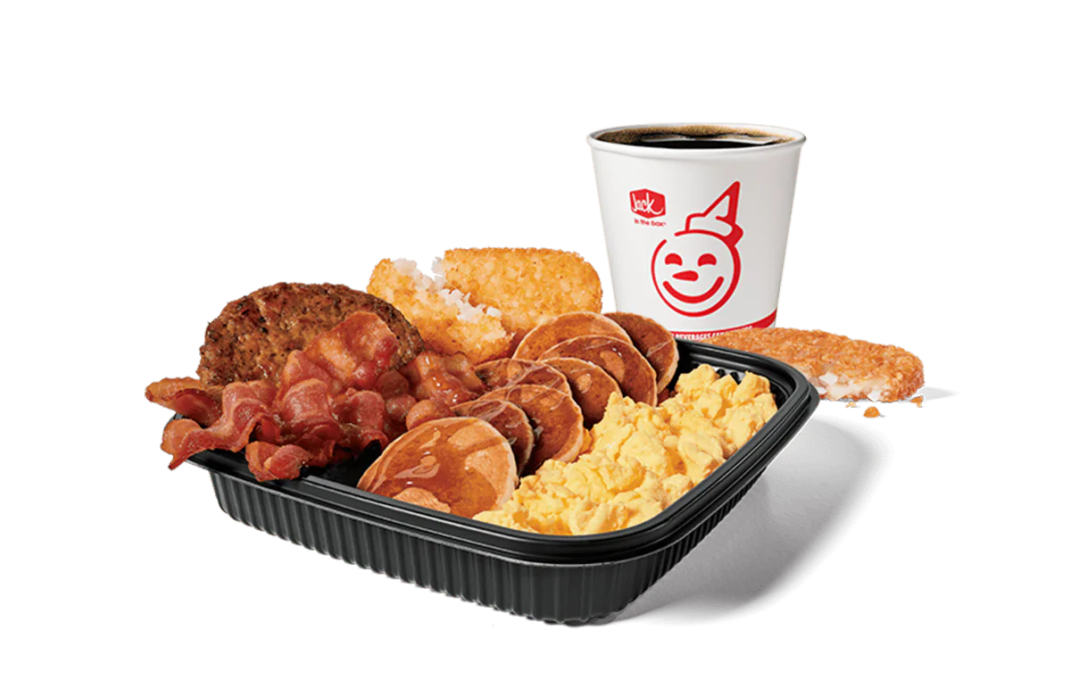 An appetizing Jumbo Breakfast Platter from Jack in the Box featuring scrambled eggs, bacon, sausage, hash browns, and mini pancakes, served with a cup of hot coffee. The meal is set against a transparent background, showcasing a hearty start to the day.