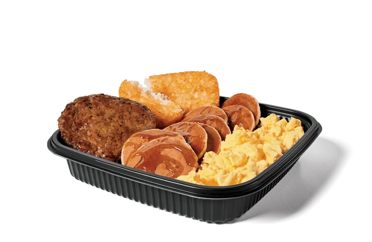 Image of a jumbo breakfast platter containing a hearty sausage patty, fluffy scrambled eggs, crisp hash browns, and mini pancakes drizzled with syrup, all presented in a black serving tray.