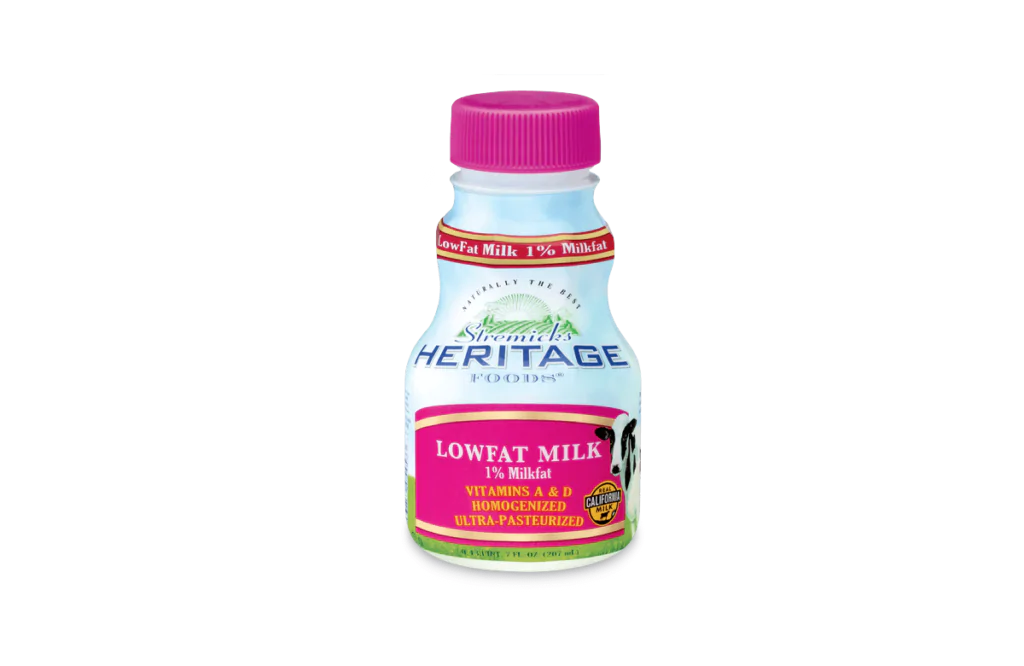 A bottle of Shamrock's Heritage Foods® Lowfat Milk with 1% milkfat, featuring a pink cap and label. The label highlights vitamins A and D, homogenized and ultra-pasteurized, with a "California Milk" certification and an image of a cow. The bottle design emphasizes health benefits and freshness.