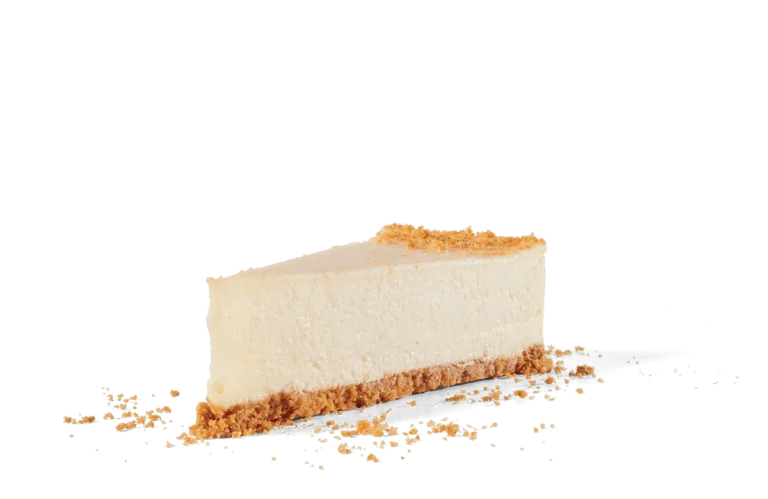 A perfect slice of New York style cheesecake with a smooth, creamy texture and a rich golden crust. The cheesecake is positioned on transparent background with crumbs scattered around the base, emphasizing its delicate yet dense composition and inviting appearance.