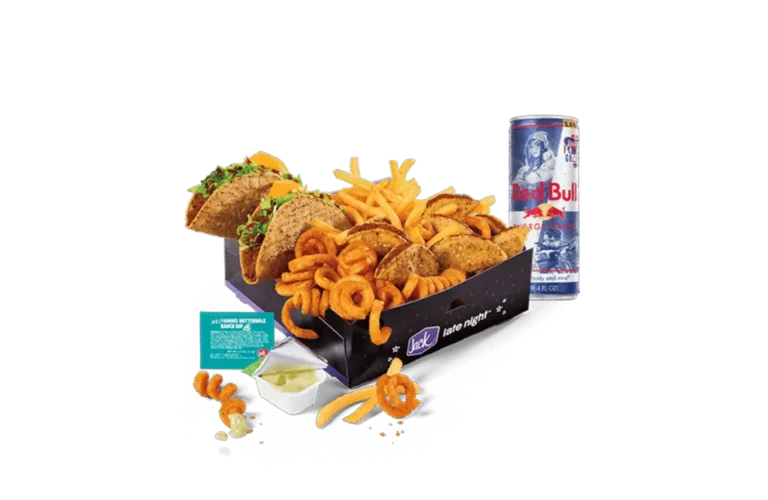 A Red Bull Gaming Box from Jack in the Box, featuring an assortment of snacks including crunchy tacos, golden fries, tiny tacos, and curly fries. The items are neatly arranged in a black box labeled "Jack late night" with stars and a moon design. A can of Red Bull Energy Drink is placed next to the box, along with a dipping sauce container and packet on the side. A few curly fries and tiny tacos are scattered around for a casual presentation.