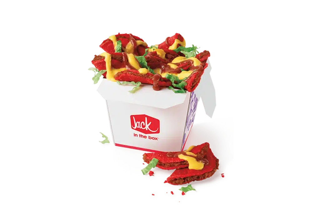 A box of sauced and loaded spicy tiny tacos from Jack in the Box, featuring red spicy mini tacos topped with melted cheese, tangy sauce, and fresh lettuce. The tacos are served in a branded white box with a red "Jack in the Box" logo, with some tacos placed outside the box for display.