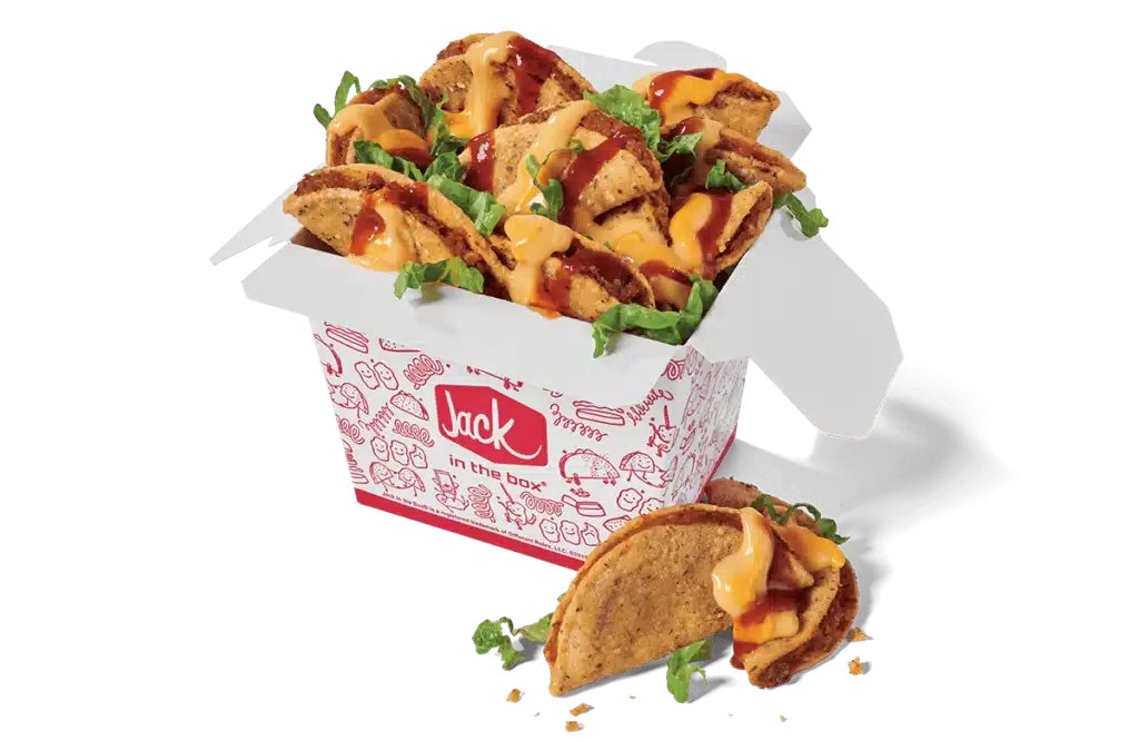 A box of sauced and loaded tiny tacos from Jack in the Box, featuring crispy mini tacos topped with shredded lettuce, drizzled with melted cheese and tangy red sauce. The tacos are served in a branded red and white box with playful illustrations. Two tacos, garnished with cheese and lettuce, are placed in front of the box for display.