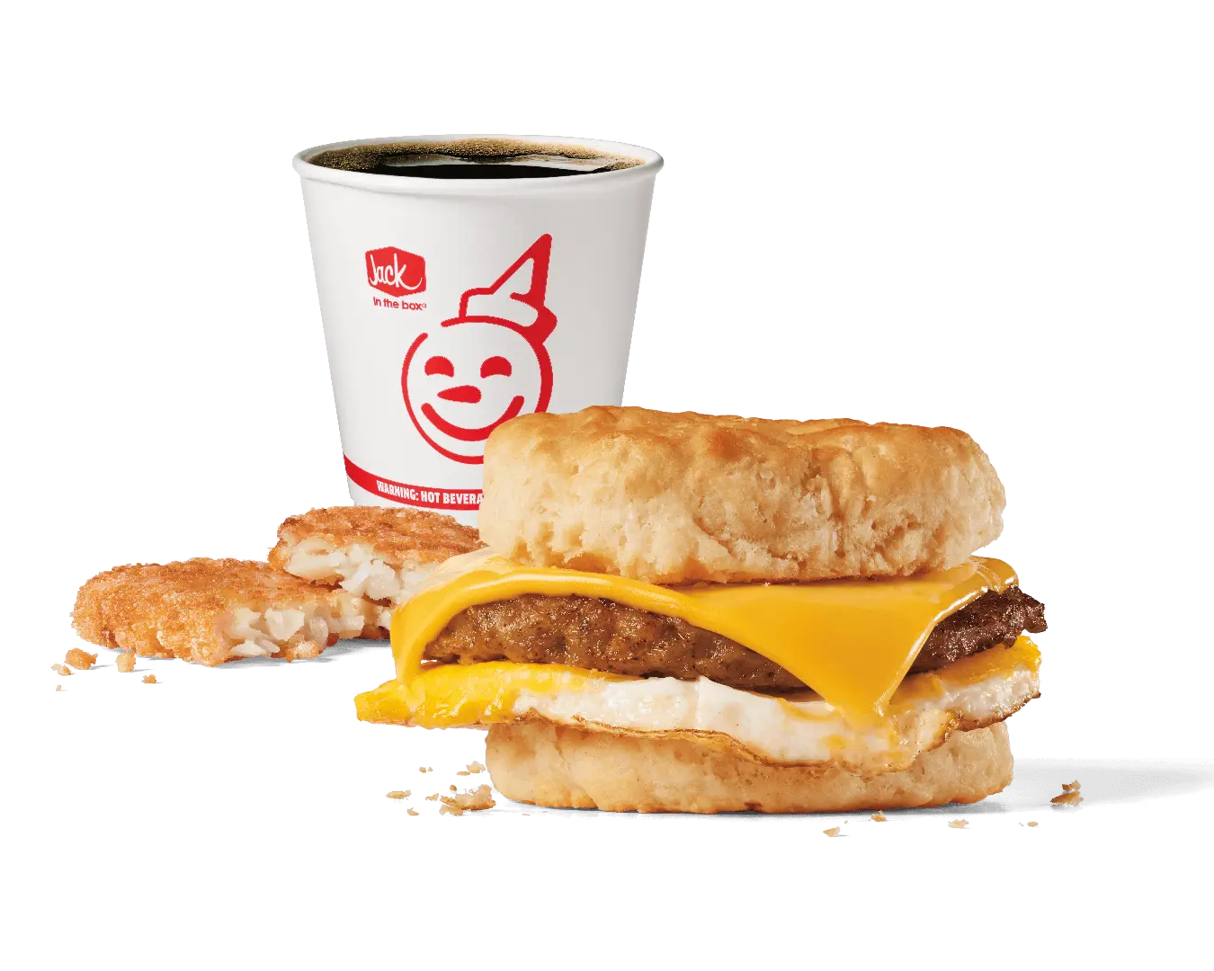 A hearty breakfast combo featuring a biscuit sandwich with a savory sausage patty, melted cheese, and a fried egg, served with a hash brown patty and a cup of hot coffee in a Jack in the Box branded cup. The background is transparent, emphasizing the meal.