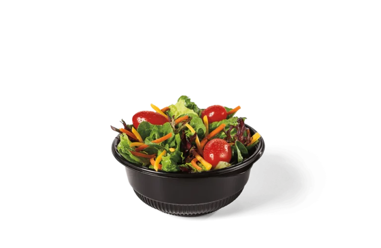 A fresh side salad in a small black bowl, featuring mixed greens, cherry tomatoes, shredded carrots, and shredded cheese.