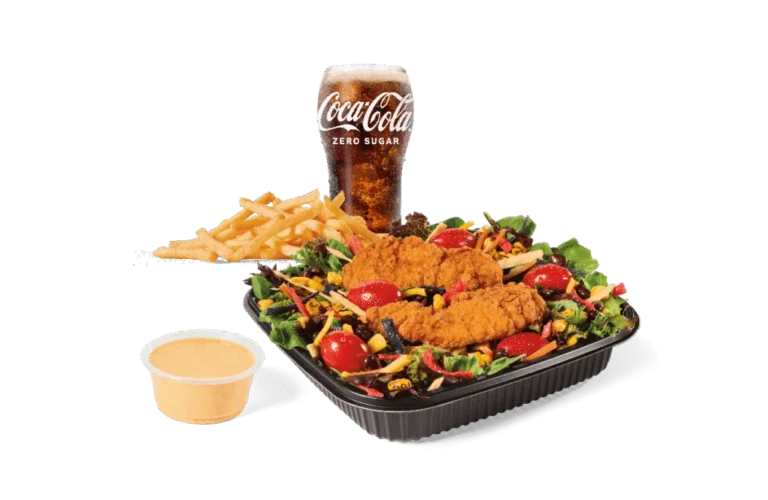 A Southwest-style salad featuring mixed greens, crispy chicken strips, cherry tomatoes, shredded cheese, colorful tortilla strips, and a side of spicy dressing. Served with a side of French fries and a Coca-Cola Zero Sugar drink.