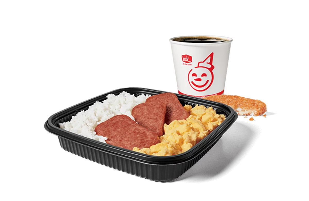 A Jack in the Box meal combo featuring a platter with white rice, slices of Spam, and scrambled eggs, accompanied by a hash brown and a coffee cup with the restaurant's smiling logo. The meal is served in a black rectangular tray, highlighting a traditional breakfast set against a transparent background.