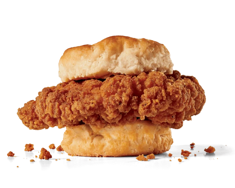 Image of a Spicy Chicken Biscuit showcasing two crispy chicken tenders with a spicy breading, nestled inside a soft, flaky biscuit, with crispy crumbs scattered around, emphasizing the texture and spice of the chicken.