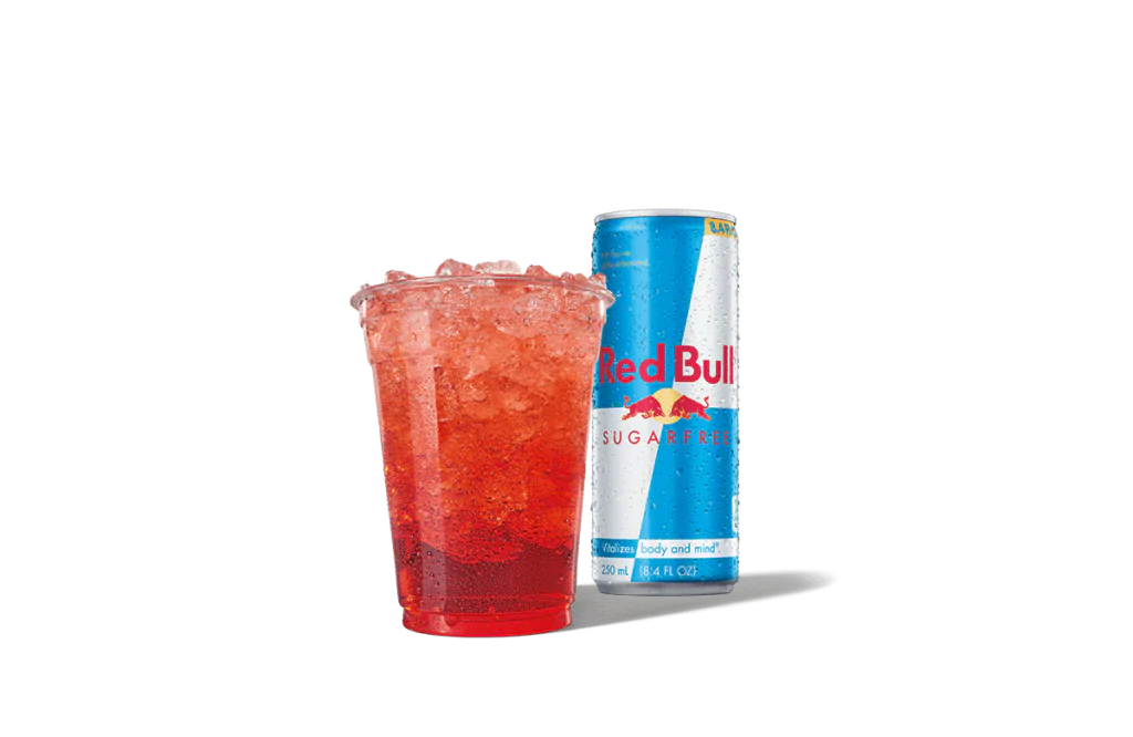 A bright red beverage called Strawberry Red Daze Red Bull® Infusion served in a clear cup filled with ice, paired with a can of Red Bull® Sugarfree in the background, offering a sugar-free energy refreshment option.