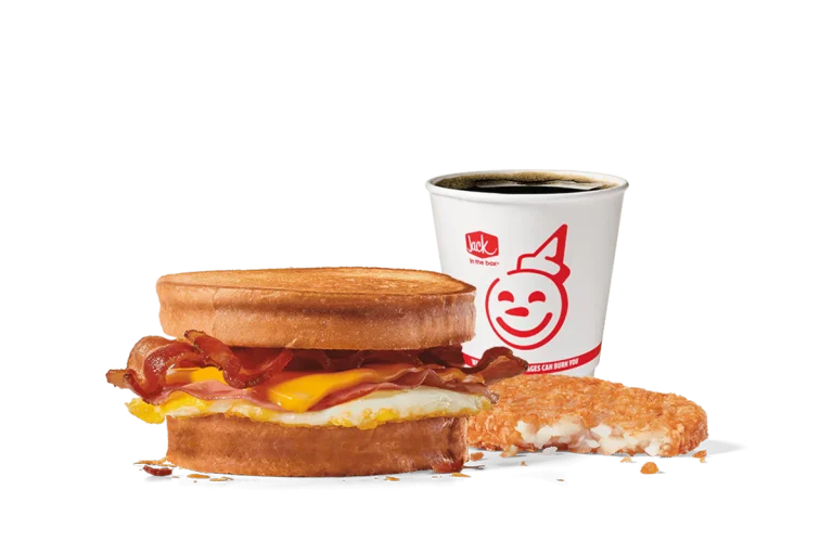 Image of the Supreme Sourdough Breakfast Sandwich Combo from Jack in the Box, featuring crispy bacon, a fried egg, and melty cheese between toasted sourdough slices. Accompanied by a hash brown and a cup of hot coffee, all set against a transparent background with the iconic smiling Jack logo.
