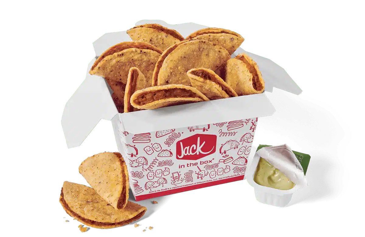 A box of Tiny Tacos from Jack in the Box. The tacos are packed in a white box decorated with red illustrations and the Jack in the Box logo. The tacos have crispy shells and are filled with seasoned meat. Some tacos are displayed outside the box for emphasis. A small dipping cup with partially opened lid, filled with green avocado lime sauce, is included on the side. The image has a transparent background.